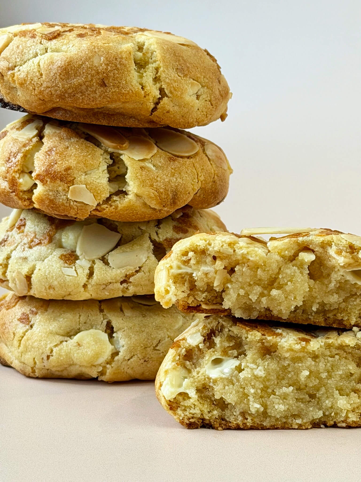 Stack of almond cookies with one cookie cut in half on a light background